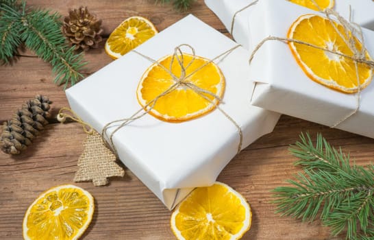 Christmas presents or gift box wrapped in kraft paper with decorations, pine cones, dry orange orange slices and fir branches on a rustic wooden background. Holiday concept