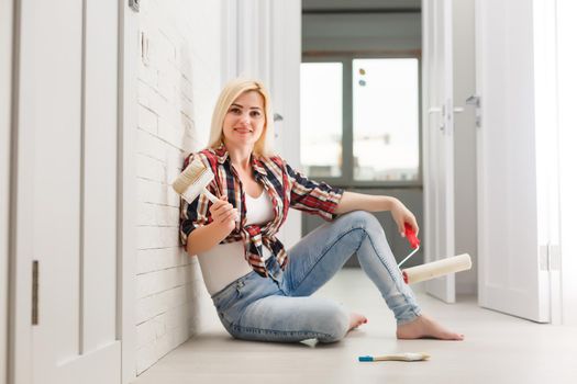 Woman painting wall in new home. Happy beautiful young woman doing wall painting. A young girl makes repairs: paints the walls with white paint using a roller.