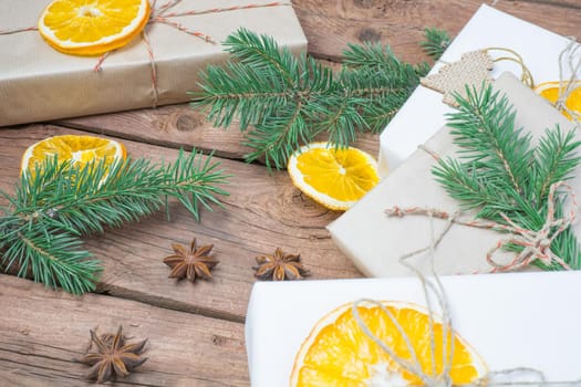Christmas presents or gift box wrapped in kraft paper with decorations, pine cones, dry orange orange slices and fir branches on a rustic wooden background. Holiday concept.
