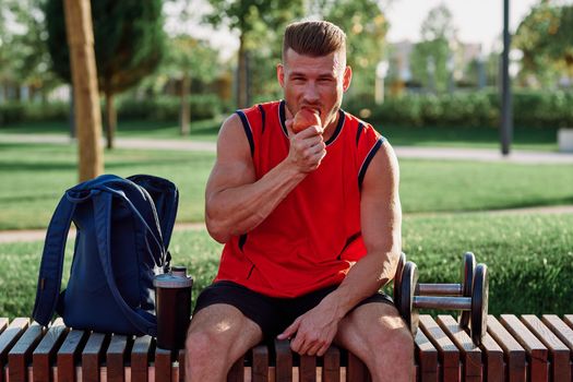 sporty man resting in the park on a bench having a snack. High quality photo