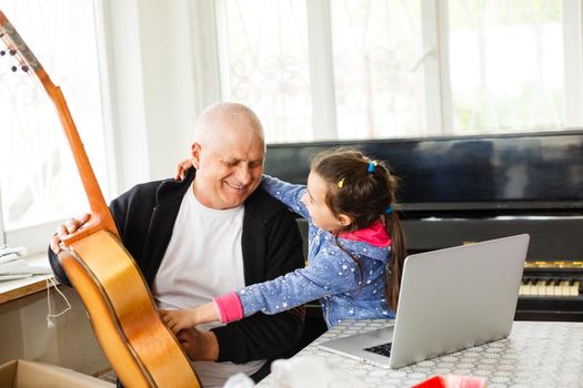 little girl plays piano together with grandfather, learning online on a laptop