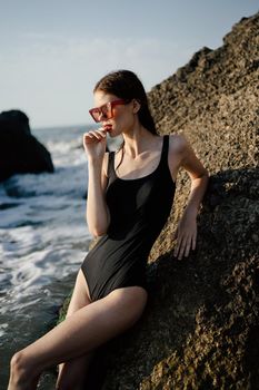 woman in swimsuit sunglasses ocean rocks posing. High quality photo