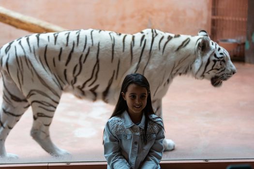 little girl and white tiger behind glass at the zoo