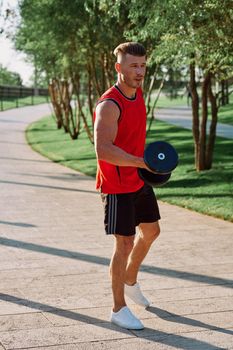 athletic man with dumbbells in his hands outdoors in the park. High quality photo
