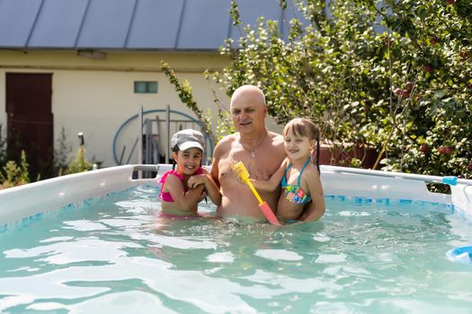 Happy active grandfather with grandchildren having fun together in swimming pool