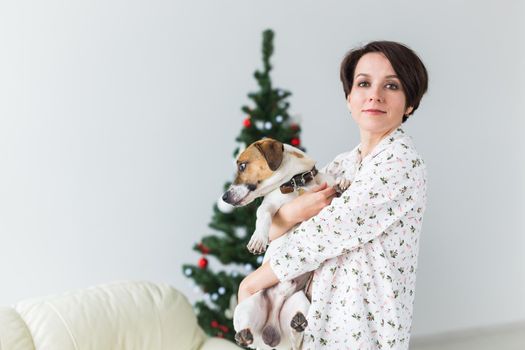 Happy woman with dog. Christmas tree with presents under it. Decorated living room.