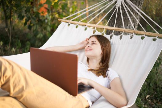 woman outdoors with laptop lies in hammock leisure technology. High quality photo