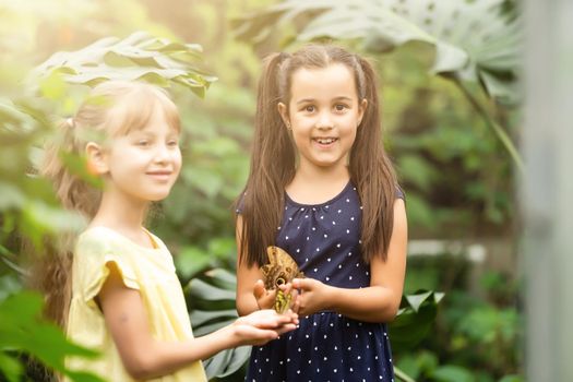 two little girls with butterflies in a greenhouse