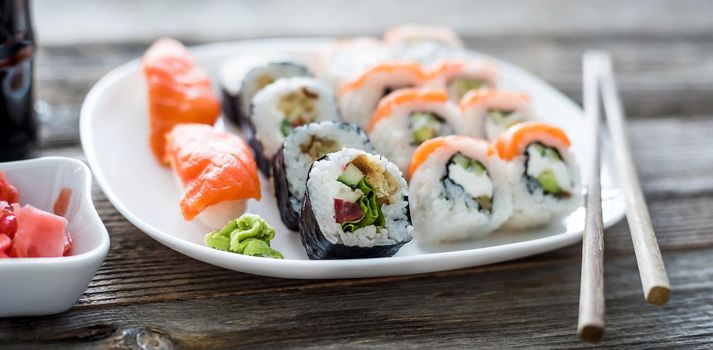 various sushi on white plate with chopsticks on wooden background