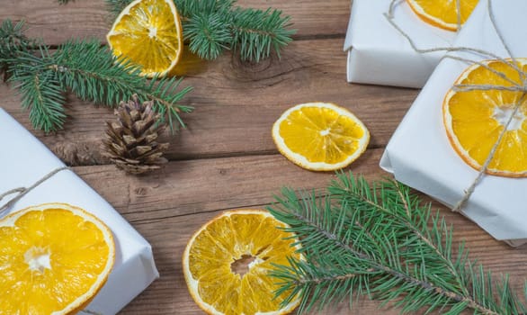 Christmas presents or gift box wrapped in kraft paper with decorations, pine cones, dried orange orange slices and fir branches on a rustic wooden background. Holiday concept