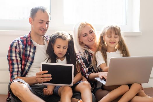 Happy family concept. Beautiful mother and handsome father with their daughters spending time together at home and lying on bed with laptop.