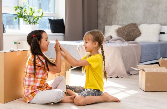 Happy family in living room. Preschool daughters sitting and help unpacking cardboard boxes belongings. Buy real estate, relocation at new modern house