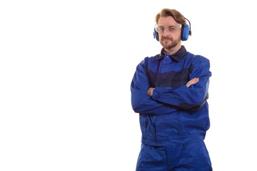 worker in safety glasses and headphones stands with his arms crossed over his chest.