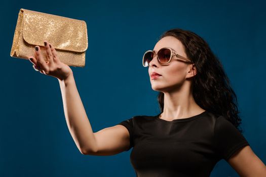beautiful girl in a black dress with a golden clutch on blue background