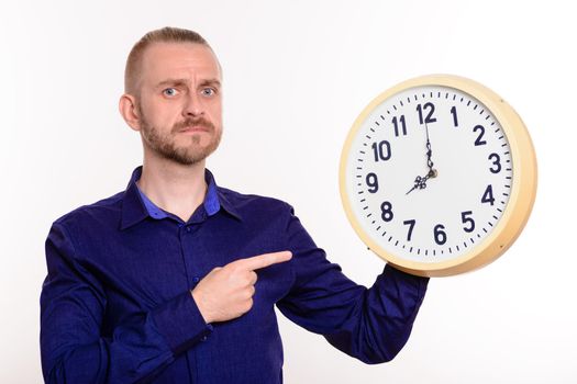 Strict man holding a large wall clock and points a finger at themon white background