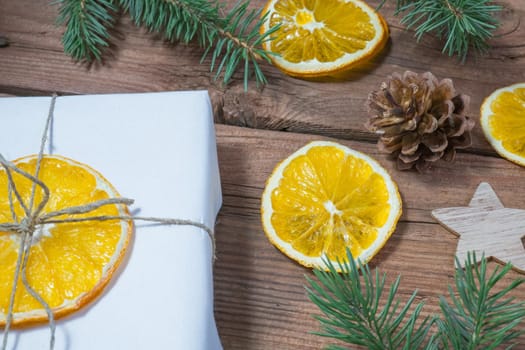 Christmas presents or gift box wrapped in kraft paper with decorations, pine cones, dried orange orange slices and fir branches on a rustic wooden background. Holiday concept