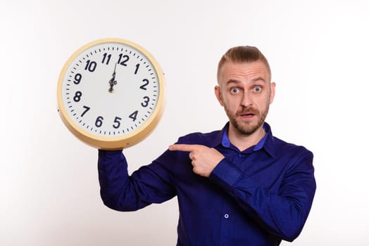 A stylish man holds a large wall clock in his hands and points to them with his finger on white background