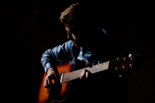 High contrast portrait of bearded man in plaid shirt playing acoustic guitar.