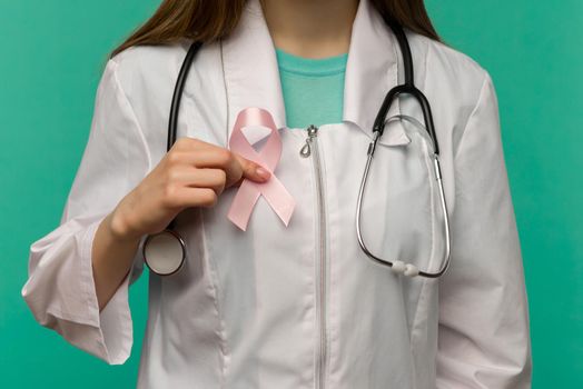 Pink ribbon for breast cancer awareness in woman doctor's hand on blue background