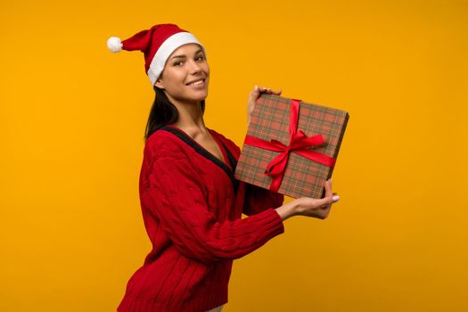 Happy excited young woman in santa claus hat with gift box over yellow background - image