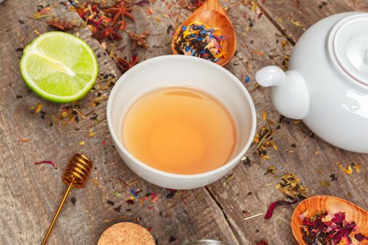cups of healthy herbal tea with cinnamon, dried rose and camomile flowers in spoons over wooden background, top view