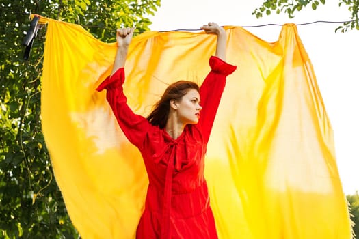 woman in a red dress with hands raised up yellow fabric nature. High quality photo