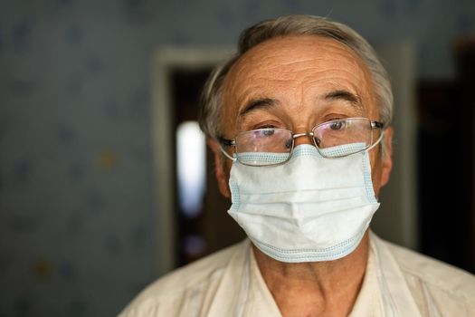 Coronavirus quarantine. Senior man wearing protective mask behind the window stay at home to avoid contagion by COVID-19 - responsibility and prevention concept