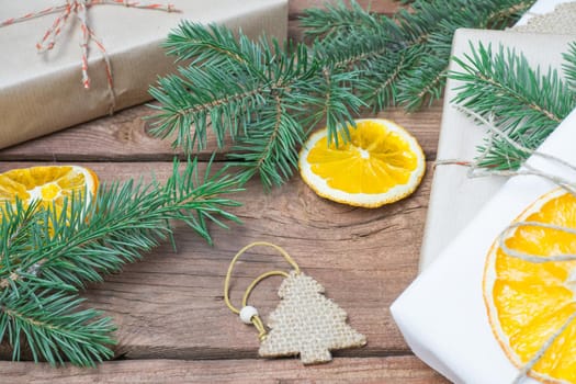 Christmas presents or gift box wrapped in kraft paper with decorations, pine cones, dry orange orange slices and fir branches on a rustic wooden background. Holiday concept.