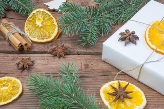 Christmas presents or gift box wrapped in kraft paper with decorations, pine cones, dry orange orange slices, cinnamon and fir branches on a rustic wooden background. Holiday concept