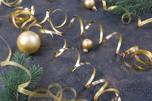 Christmas composition of yellow Christmas balls, fir branches and a gold ribbon on a black with gold embossed background