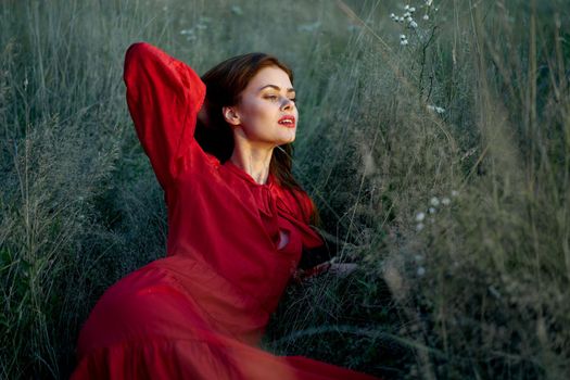 pretty woman in red dress lies on the grass nature sun. High quality photo