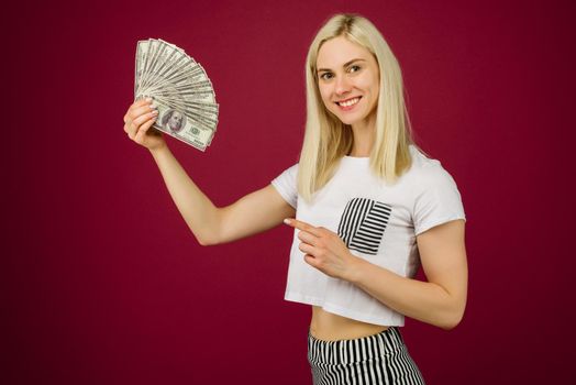 Young woman pointing towards a stack of money with her finger isolated on ruby background - Image