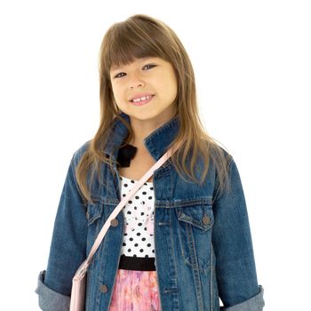 Portrait of happy girl in stylish outfit. Beautiful smiling brown eyed preteen girl wearing denim jacket posing against white background with crossbody shoulder bag