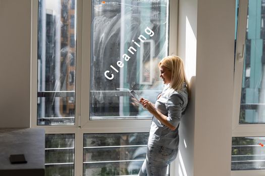 woman with tablet looking for cleaning to wash dirty window