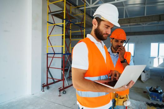 Two specialists supervisors in hardhats using laptop at construction site for work, close up