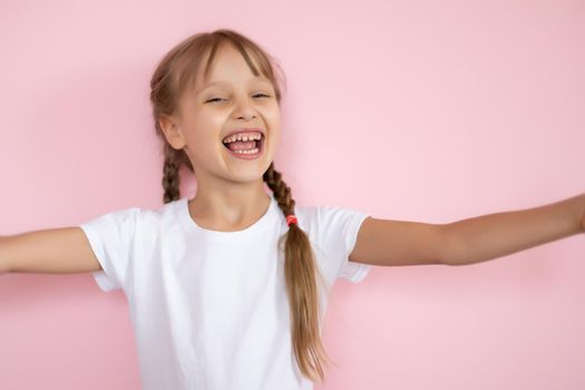 Beautiful little blonde girl with long hair in white T-shirt smiling on a pink background