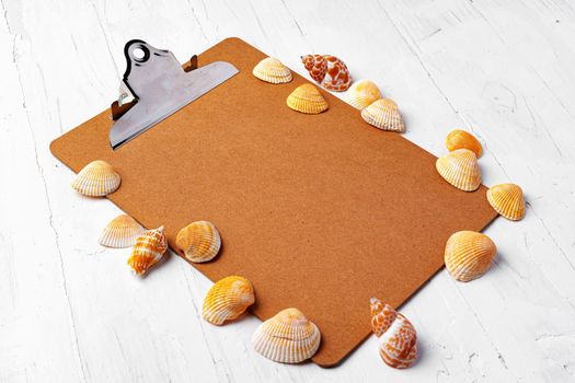 Clipboard with sea shells on white wooden table close up, copy space.
