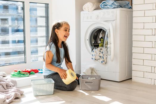 Beautiful child girl little helper is having fun and playing while doing laundry at home.