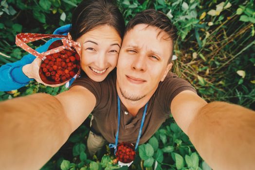 Happy young couple in love taking self-portrait in summer garden with raspberries