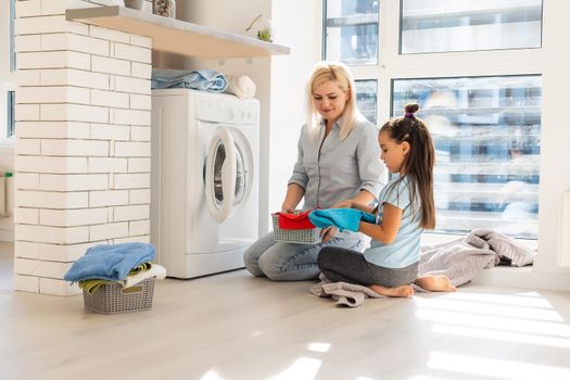 Happy housewife and her daughter with linen near washing machine