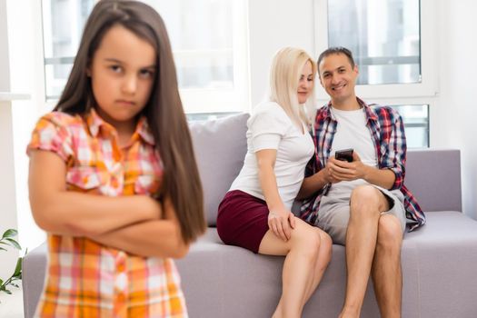 Sad girl hearing her parents while sitting on sofa at home