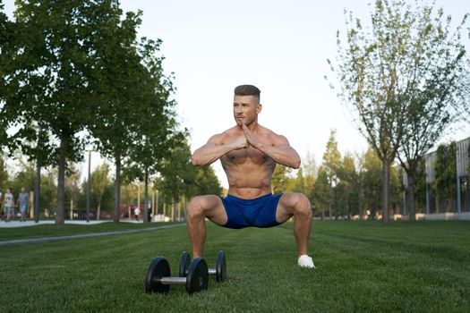 Muscled man in the park training with dumbbells. High quality photo
