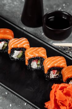 A set of sushi rolls Philadelphia with red fish, cream cheese and black rise lies in a plate boat. Sushi rolls on a gray background.