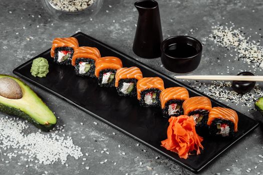 A set of sushi rolls Philadelphia with red fish, cream cheese and black rise lies in a plate boat. Sushi rolls on a gray background.