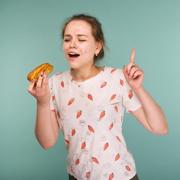 Portrait of pimply teen girl wants to eat eclair cake on blue background