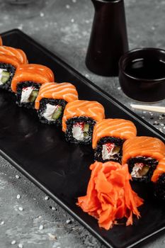 A set of sushi rolls Philadelphia with red fish, cream cheese and black rise lies in a plate boat. Sushi rolls on a gray background.