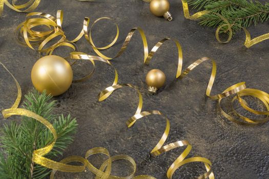 Christmas composition of yellow Christmas balls, fir branches and a gold ribbon on a black with gold embossed background