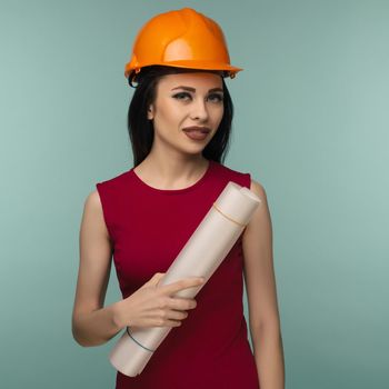 Young female engineer in orange helmet with drawings isolated on blue background - Image