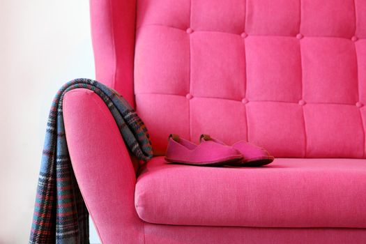 Pink slippers and blanket on a pink coach. Still life details in home interior of living room. Cozy home interior, home comfort concept, gender free interior. Modern interior in the room