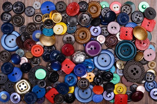 old multi-colored buttons scattered on a wooden background.